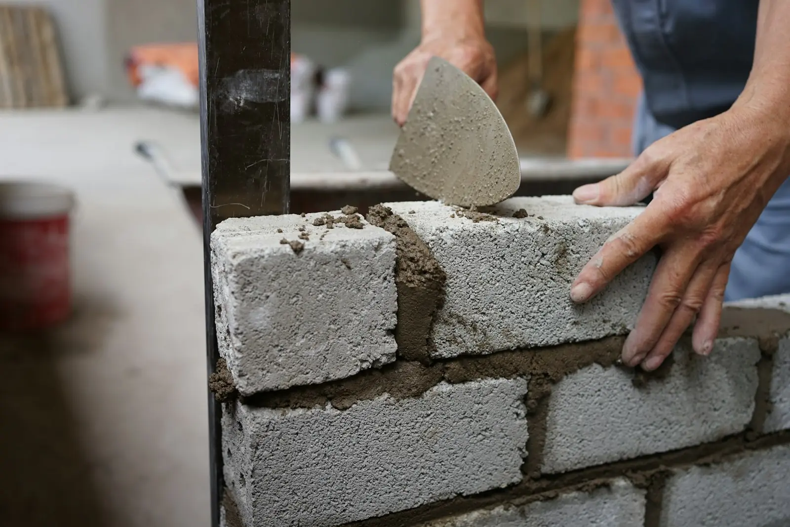 A bricklayer's hands setting a concrete block on fresh mortar
