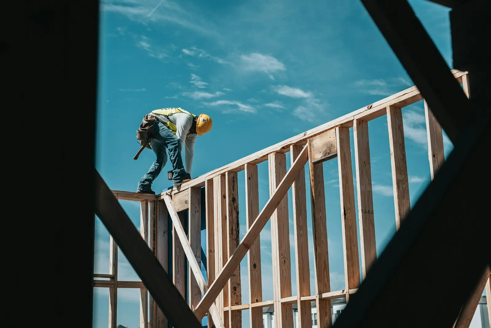 Builder in a hard hat and hi-vis vest working on top of a timber wall frame