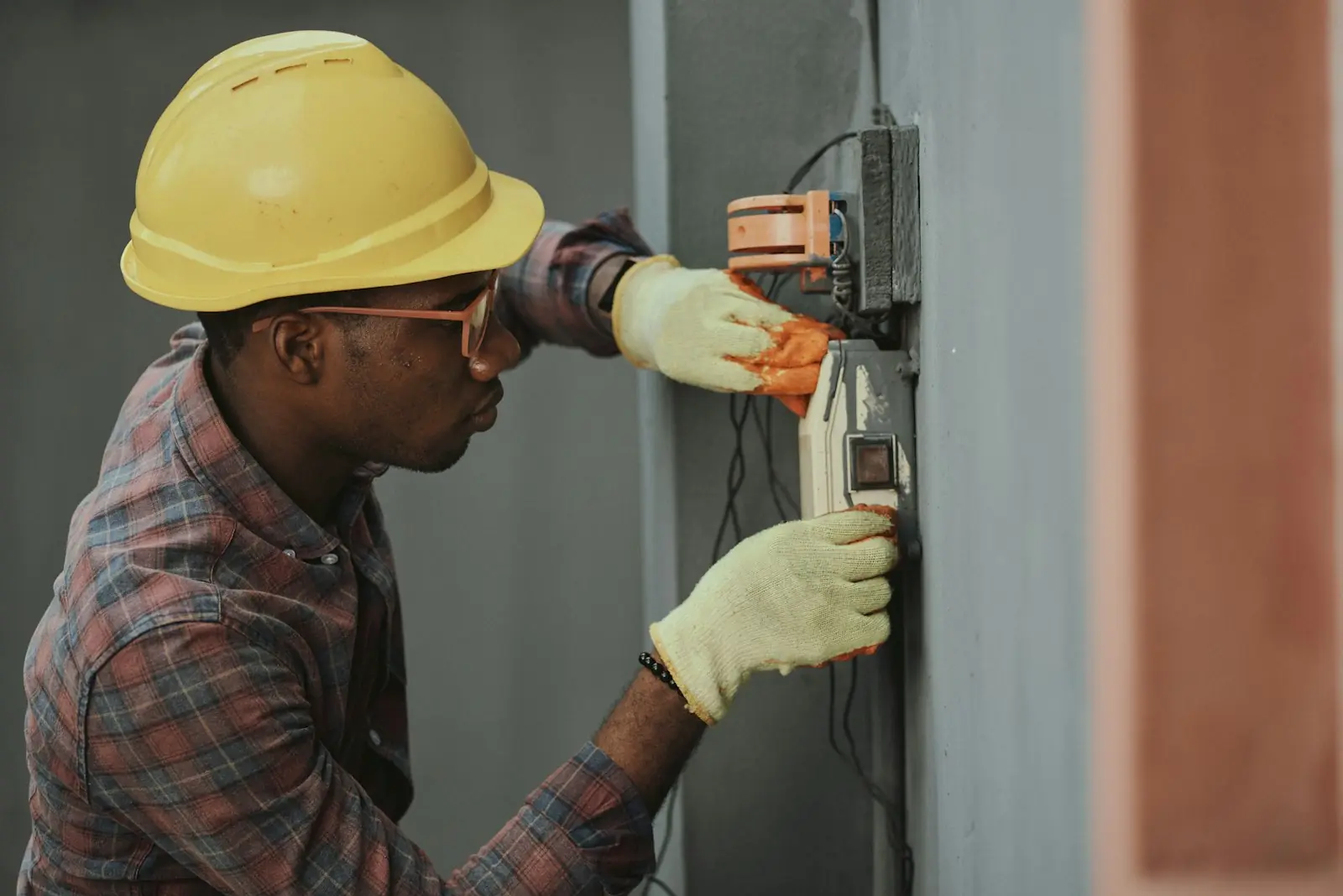 Electrician in a hard hat and gloves wiring a wall-mounted switch box