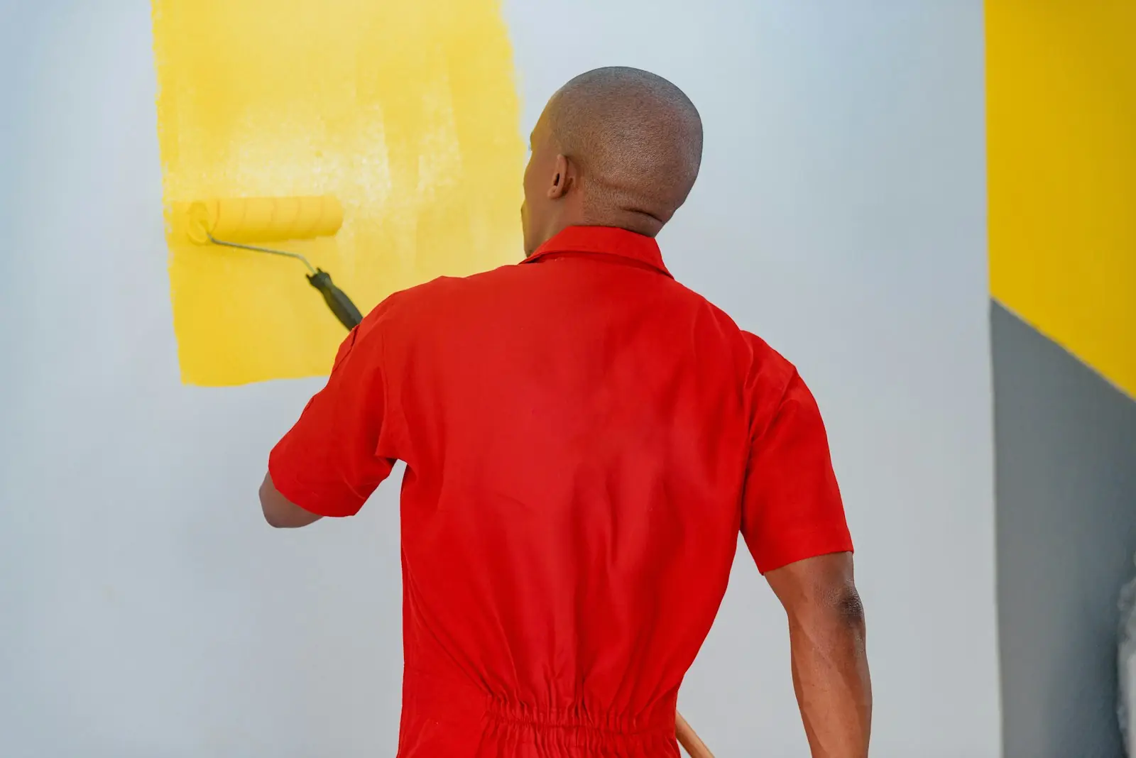 Painter in red overalls rolling yellow paint onto a white wall