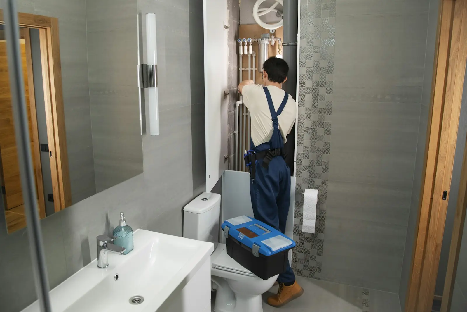 Plumber in overalls working on pipework inside a bathroom service cupboard