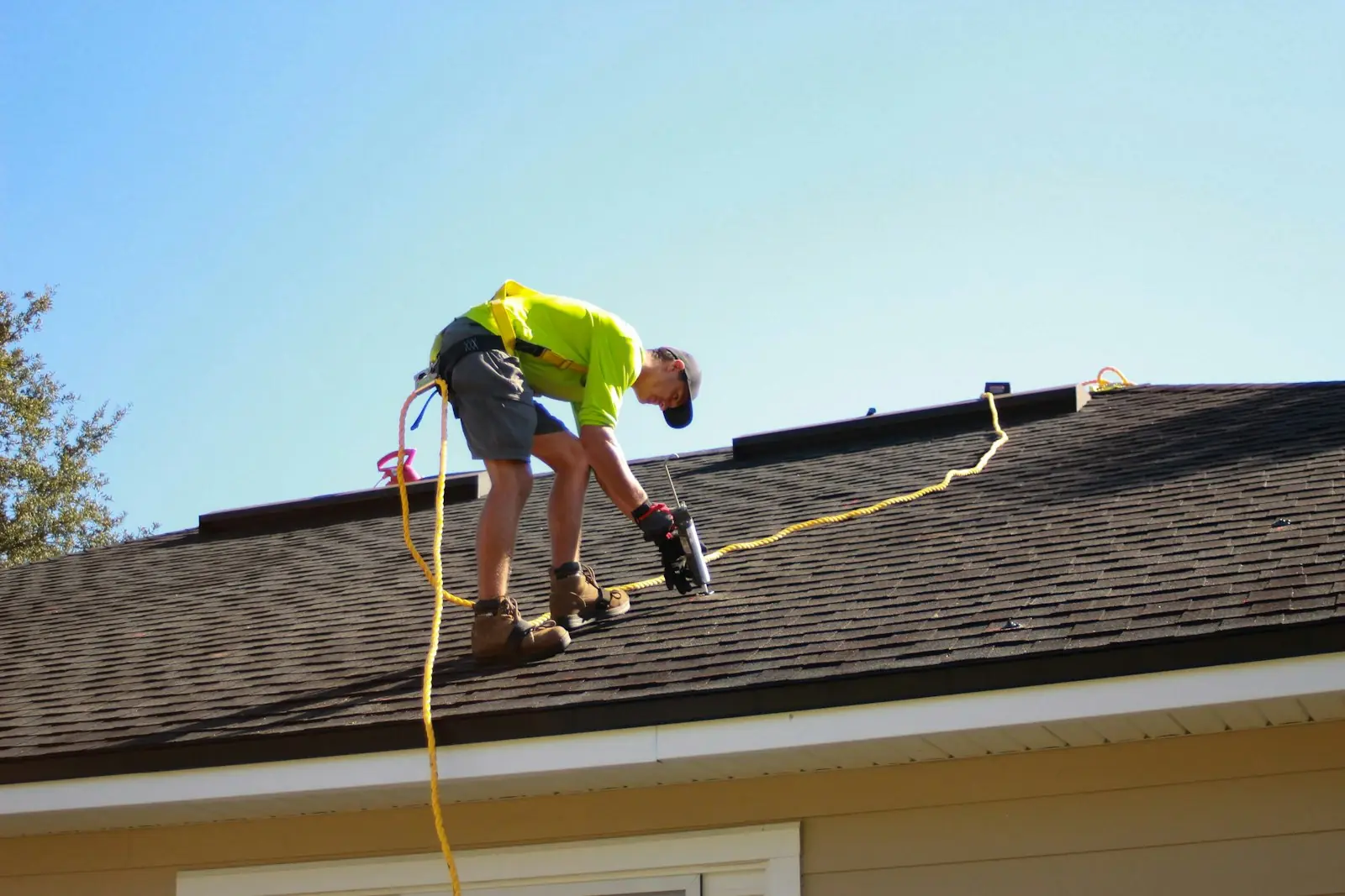 Roofer in a hi-vis shirt and safety harness sealing a shingle roof