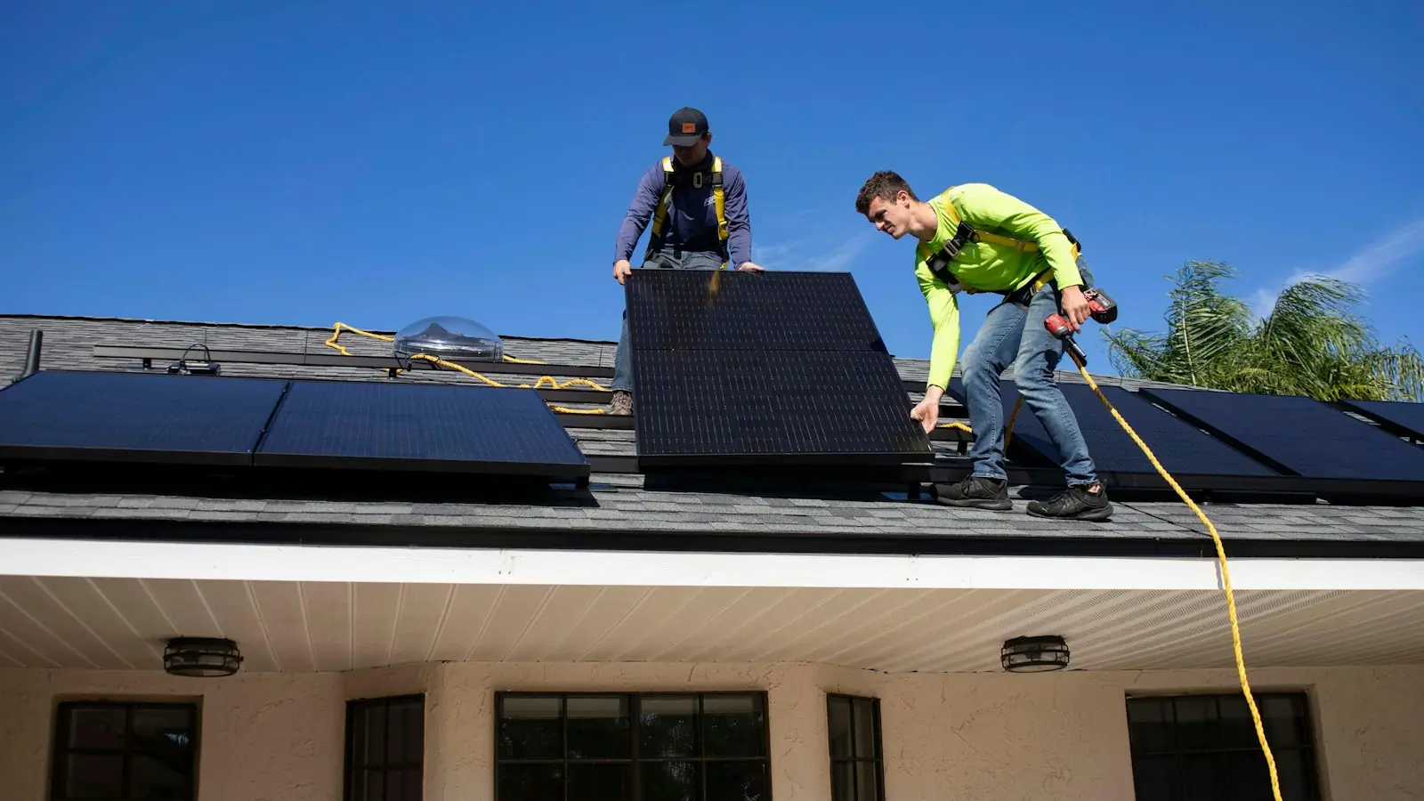 Two harnessed installers lowering a solar panel into place on a house roof